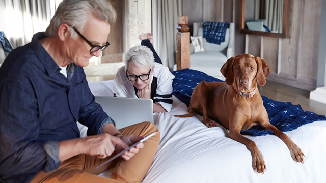A man on a table and a woman on a laptop on the bed with their dog
